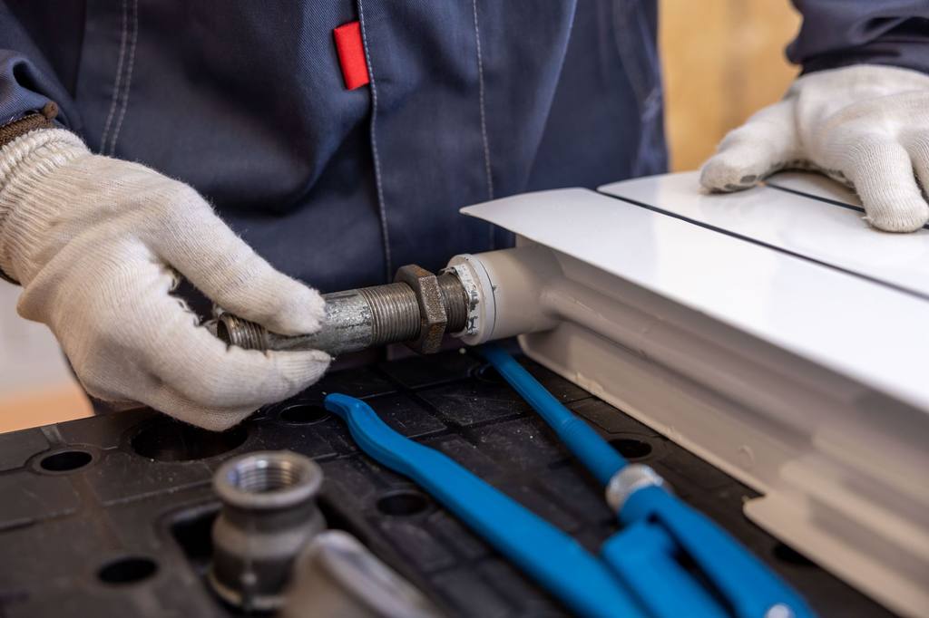 Heating engineer in work gloves fitting a pipe connection to a white radiator